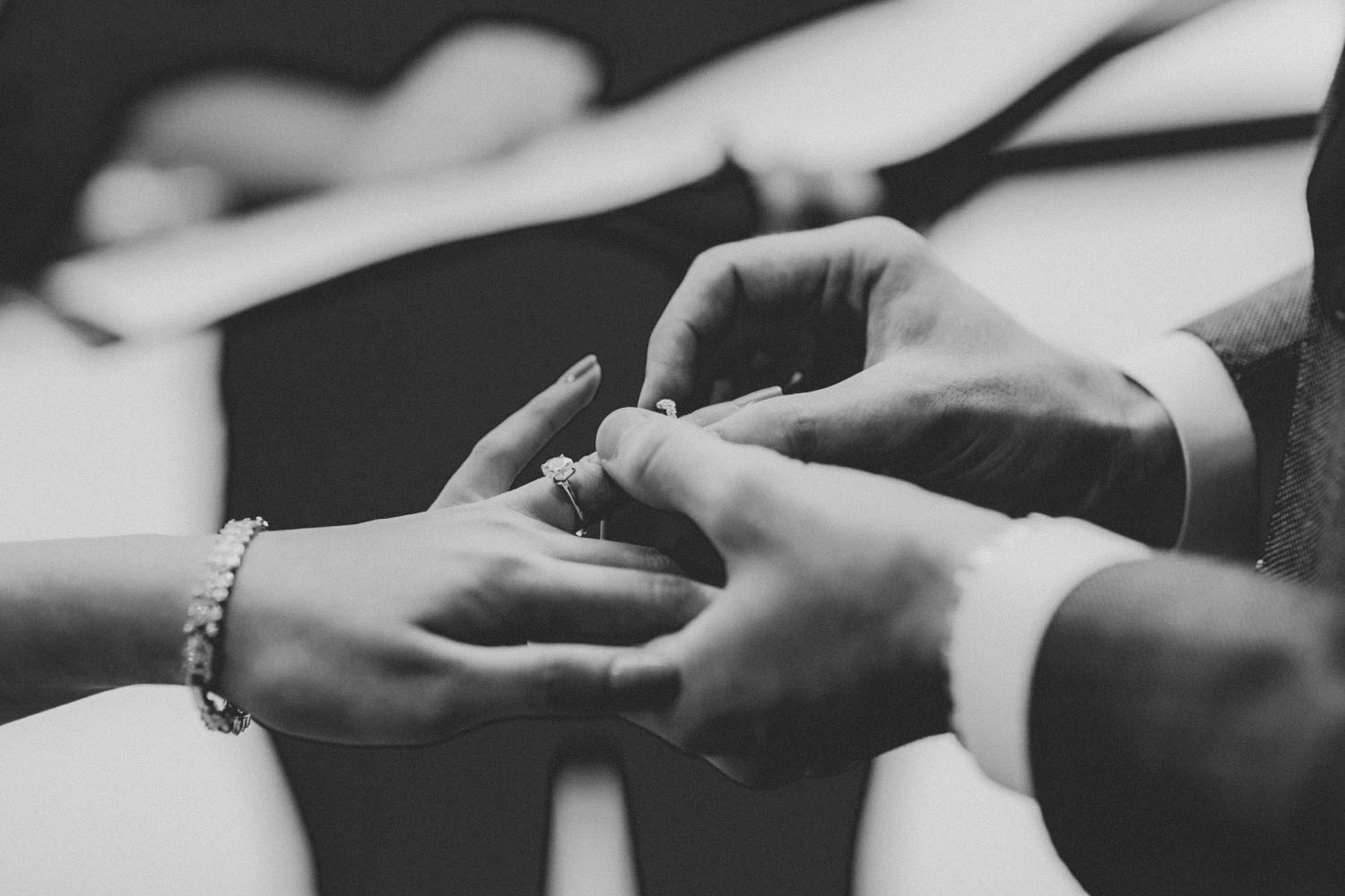 Black and white close-up of wedding rings being placed during a ceremony